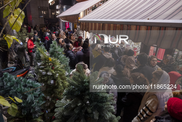 A crowd walks past Christmas trees being placed on a sidewalk and shops decorated for Christmas shopping in downtown Tehran, Iran, on Decemb...