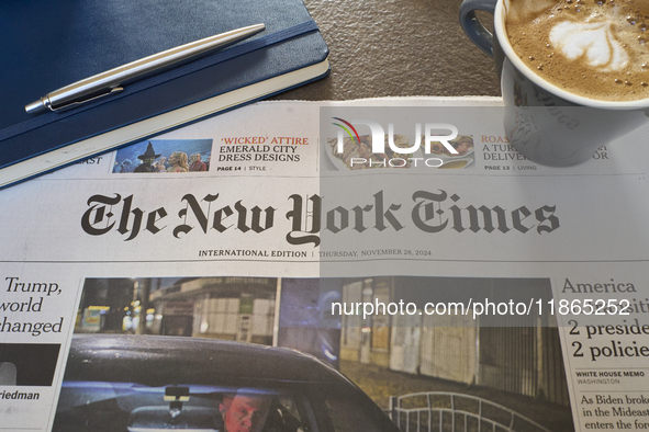 A cozy morning scene features the international edition of The New York Times alongside a cup of cappuccino with latte art and a notebook. T...