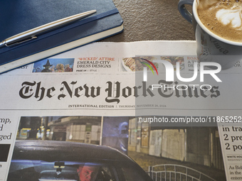 A cozy morning scene features the international edition of The New York Times alongside a cup of cappuccino with latte art and a notebook. T...