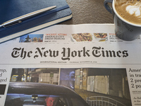 A cozy morning scene features the international edition of The New York Times alongside a cup of cappuccino with latte art and a notebook. T...