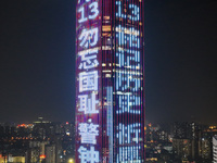 A large LED screen on the exterior wall of a building displays a propaganda slogan to commemorate the innocent victims of the Nanjing Massac...