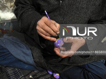 In Srinagar, Kashmir, India, on December 14, 2024, Kashmiri artisan Muhammad Akhtar Mir paints Christmas gift items at his workshop ahead of...