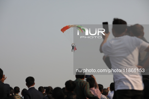 People watch as an Indian army paratrooper jumps from a plane carrying a flag during the full dress rehearsal ahead of ''Vijay Diwas,'' a ce...