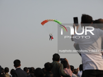 People watch as an Indian army paratrooper jumps from a plane carrying a flag during the full dress rehearsal ahead of ''Vijay Diwas,'' a ce...