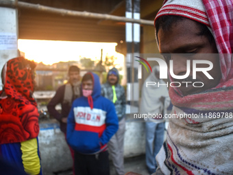 People stand beside the road on an early winter morning in Kolkata, India, on December 15, 2024. (