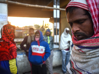 People stand beside the road on an early winter morning in Kolkata, India, on December 15, 2024. (