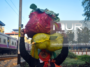 A vegetable seller carries vegetables on his head and goes towards the market in Kolkata, India, on December 15, 2024. (