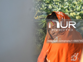 A woman covers her face with a woolen shawl while sitting in the sunlight on an early winter morning in Kolkata, India, on December 15, 2024...