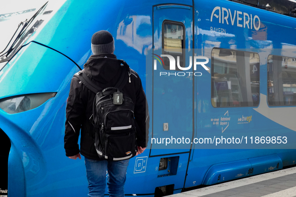 A traveler carrying a backpack waits next to an Arverio regional train at Augsburg Central Station in Bavaria, Germany, on December 14, 2024...