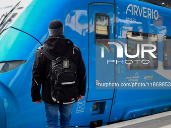 A traveler carrying a backpack waits next to an Arverio regional train at Augsburg Central Station in Bavaria, Germany, on December 14, 2024...