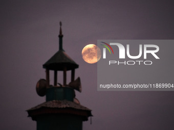 The final full moon, or cold moon, rises behind the minaret of a mosque in Srinagar, Kashmir, India, on December 14, 2024. In India, reports...