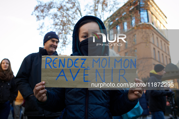 A child holds a placard reading 'Give me back my future'. Between 100 and 1500 people gather in Toulouse, France, on December 15, 2024, to p...