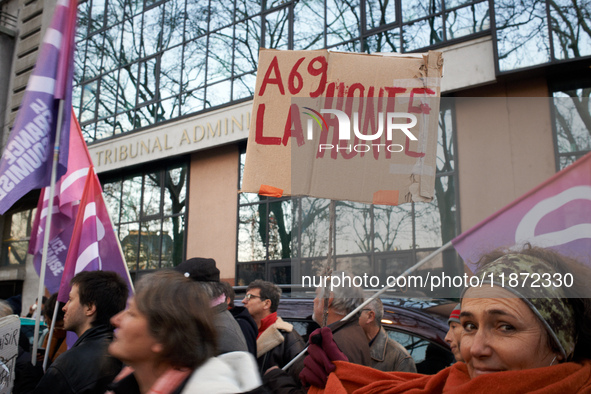 A woman holds a cardboard sign reading 'Shame on the A69' in front of the Administrative Court of Toulouse. Between 1,000 and 1,500 people g...