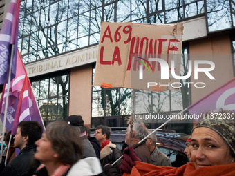 A woman holds a cardboard sign reading 'Shame on the A69' in front of the Administrative Court of Toulouse. Between 1,000 and 1,500 people g...