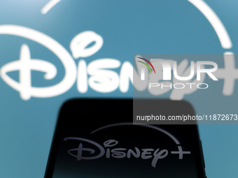 The Disney Plus logo appears on the screen of a smartphone and in the background on the computer screen in Reno, United States, on December...