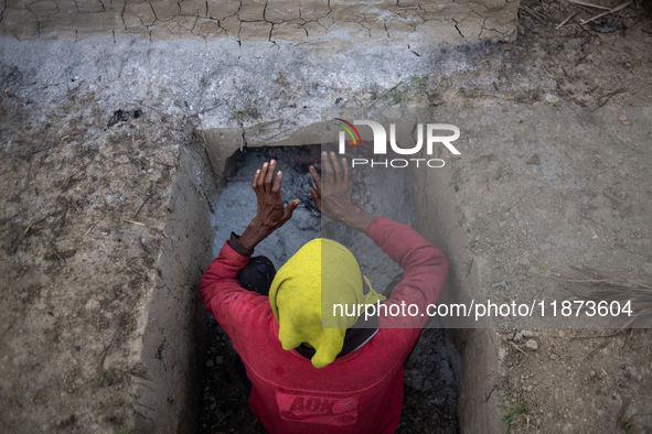 A worker warms himself as others prepare date jaggery after collecting juice from date palm trees in Magura, Bangladesh, on January 16, 2024...