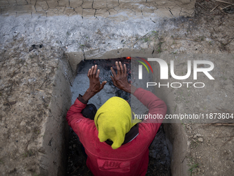 A worker warms himself as others prepare date jaggery after collecting juice from date palm trees in Magura, Bangladesh, on January 16, 2024...