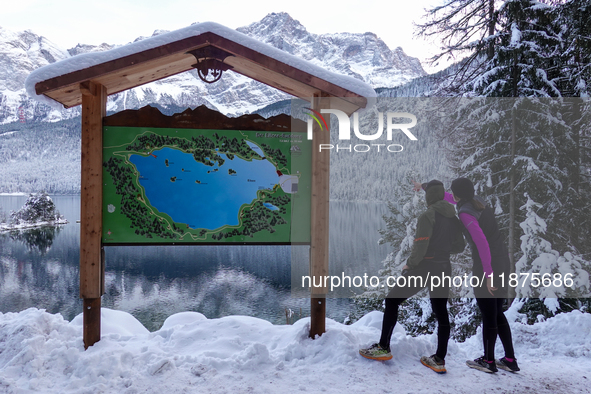 Visitors consult a trail map during a winter hike at Lake Eibsee in Grainau, Bavaria, Germany, on December 13, 2024. Two hikers stand in fro...