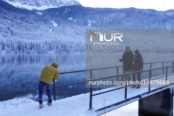 Visitors explore the snow-covered bridge and frozen landscape of Lake Eibsee in Grainau, Bavaria, Germany, on December 13, 2024. The serene...