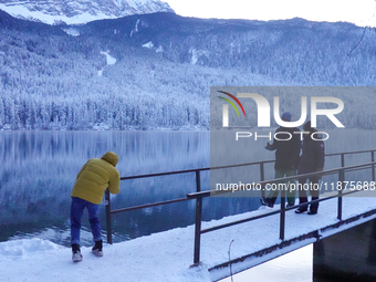 Visitors explore the snow-covered bridge and frozen landscape of Lake Eibsee in Grainau, Bavaria, Germany, on December 13, 2024. The serene...