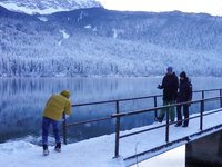 Visitors explore the snow-covered bridge and frozen landscape of Lake Eibsee in Grainau, Bavaria, Germany, on December 13, 2024. The serene...