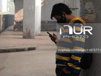 A young man wearing a face mask looks at his phone as the air quality index slips to the 'severe' category in New Delhi, India, on December...