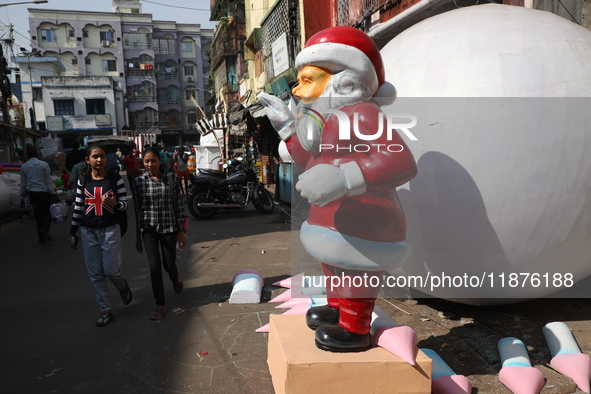 Women walk past a giant model of Santa Claus made of polystyrene at a roadside workshop ahead of Christmas celebrations in Kolkata, India, o...