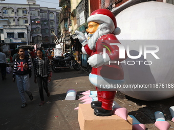 Women walk past a giant model of Santa Claus made of polystyrene at a roadside workshop ahead of Christmas celebrations in Kolkata, India, o...