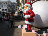 Women walk past a giant model of Santa Claus made of polystyrene at a roadside workshop ahead of Christmas celebrations in Kolkata, India, o...