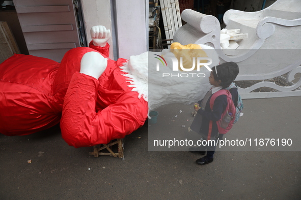 School students look at a giant model of Santa Claus made of polystyrene at a roadside workshop ahead of Christmas celebrations in Kolkata,...