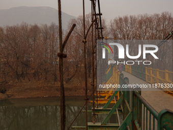 A girl walks on a metal pedestrian bridge on a cold winter day in Baramulla, Jammu and Kashmir, India, on December 17, 2024. (