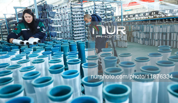 Workers sort warp threads for industrial textiles at a textile production line in Zhangye, China, on December 17, 2024. 