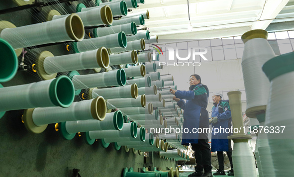 Workers sort warp threads for industrial textiles at a textile production line in Zhangye, China, on December 17, 2024. 