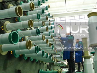 Workers sort warp threads for industrial textiles at a textile production line in Zhangye, China, on December 17, 2024. (