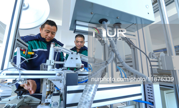 Workers check the production of air filter bags at an automated production line for textile tube filter bags in Zhangye, China, on December...