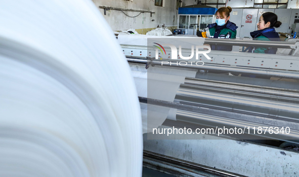 Workers work on hot-pressed rolls for industrial textiles at a textile production line in Zhangye, China, on December 17, 2024. 