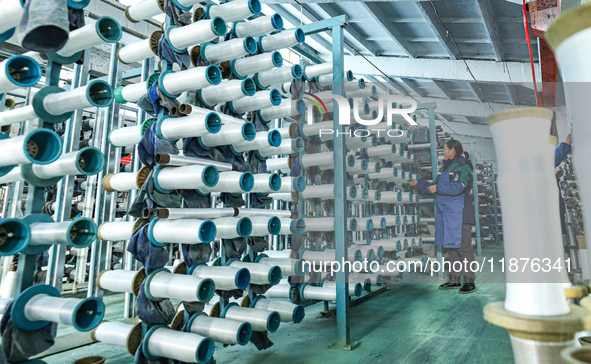 Workers sort warp threads for industrial textiles at a textile production line in Zhangye, China, on December 17, 2024. 