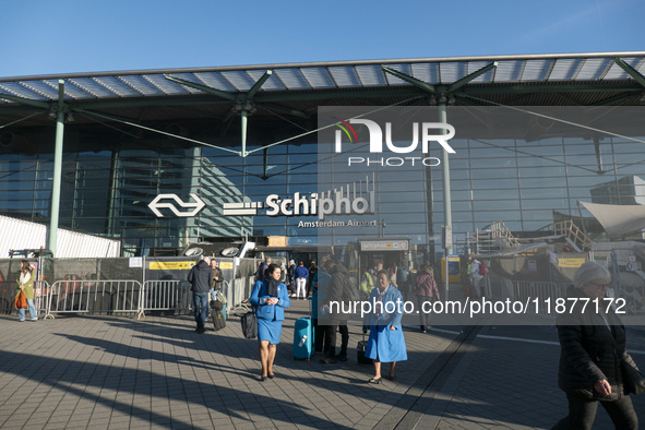 Entrance of Amsterdam Airport Schiphol AMS EHAM airport terminal with passenger and flight crew walking by and the logo inscription over the...