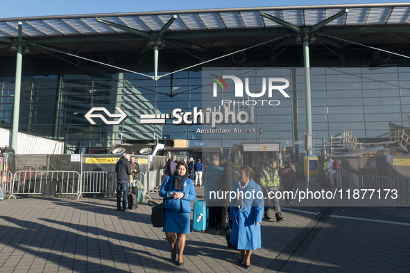 Entrance of Amsterdam Airport Schiphol AMS EHAM airport terminal with passenger and flight crew walking by and the logo inscription over the...