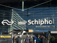 Entrance of Amsterdam Airport Schiphol AMS EHAM airport terminal with passenger and flight crew walking by and the logo inscription over the...