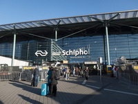 Entrance of Amsterdam Airport Schiphol AMS EHAM airport terminal with passenger and flight crew walking by and the logo inscription over the...