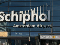 Entrance of Amsterdam Airport Schiphol AMS EHAM airport terminal with passenger and flight crew walking by and the logo inscription over the...