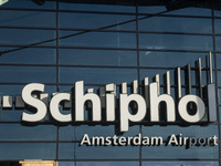 Entrance of Amsterdam Airport Schiphol AMS EHAM airport terminal with passenger and flight crew walking by and the logo inscription over the...