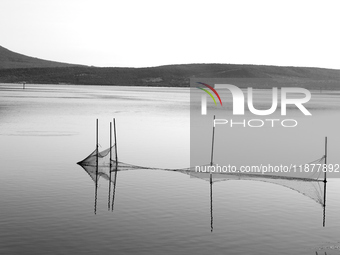 This black and white image shows the reflection of fishing nets on the still waters of a lake, in Varano Lake, Italy, on July 16, 2023. (