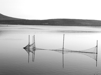 This black and white image shows the reflection of fishing nets on the still waters of a lake, in Varano Lake, Italy, on July 16, 2023. (