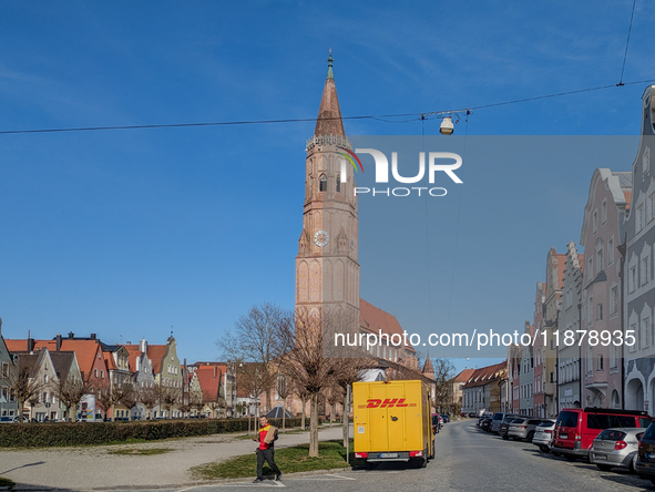 A DHL delivery van parks near a historic church in Landshut, Bavaria, Germany, on March 9, 2024. A delivery worker carries a package. 