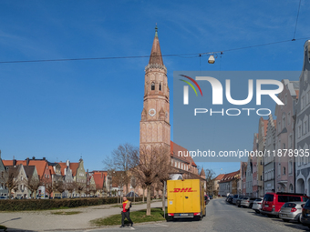 A DHL delivery van parks near a historic church in Landshut, Bavaria, Germany, on March 9, 2024. A delivery worker carries a package. (