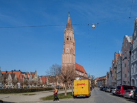 A DHL delivery van parks near a historic church in Landshut, Bavaria, Germany, on March 9, 2024. A delivery worker carries a package. (