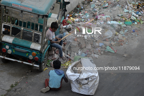 Two young child laborers collect plastic bottles and other reusable items from a roadside garbage disposal area while a worker and two schoo...