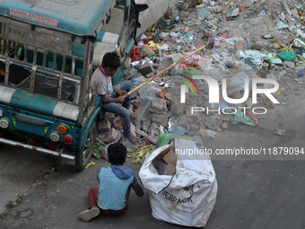 Two young child laborers collect plastic bottles and other reusable items from a roadside garbage disposal area while a worker and two schoo...